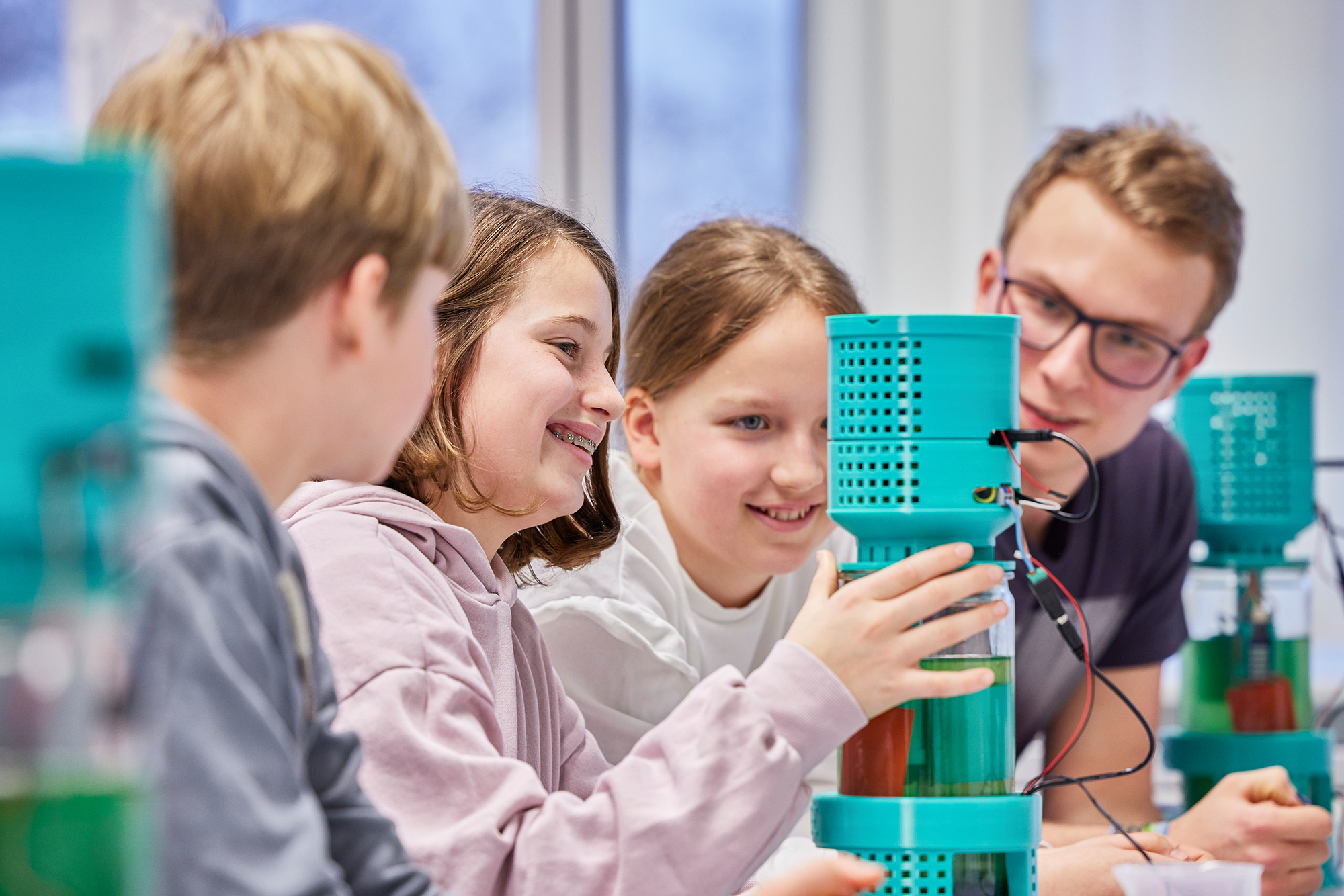 Gruppe von Schülern mit Lehrperson arbeiten an einem Fotobioreaktor, in dem Mikroalgen gezüchtet werden.