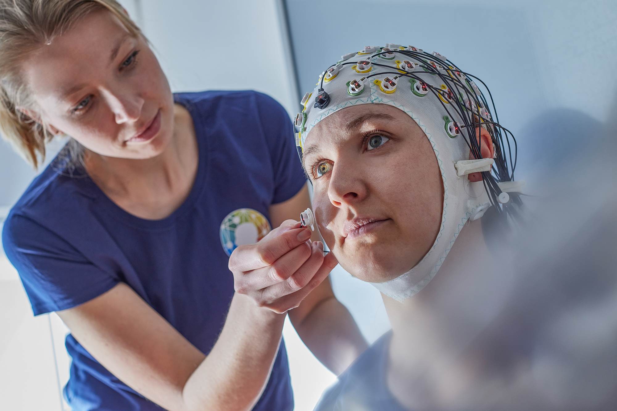 Forscherin bringt bei Probandin Elektrode an der EEG-Haube an.