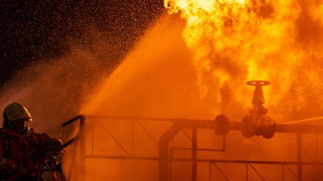 Firefighters using water fog spraying down fire from oil rig factory explosion.