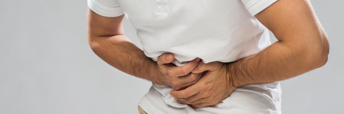 Mann krümmt sich vor Schmerzen und hält Hände vor den Bauch.