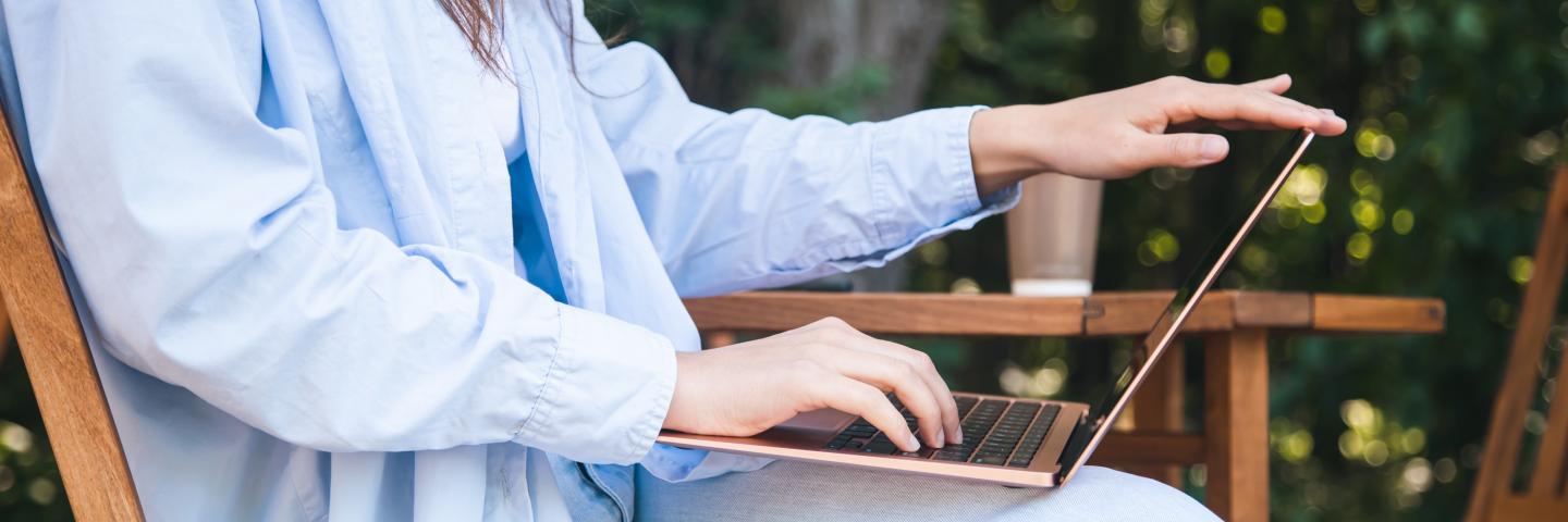 Person sitzt im Garten und hat ein Laptop auf dem Schoß