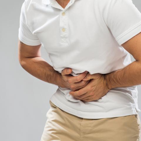 Mann krümmt sich vor Schmerzen und hält Hände vor den Bauch.